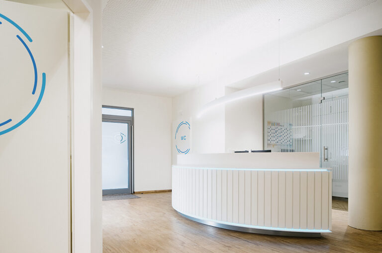 Modern heller Empfangsbereich mit geschwungenem Tresen und Holzboden in Weiß und Beige