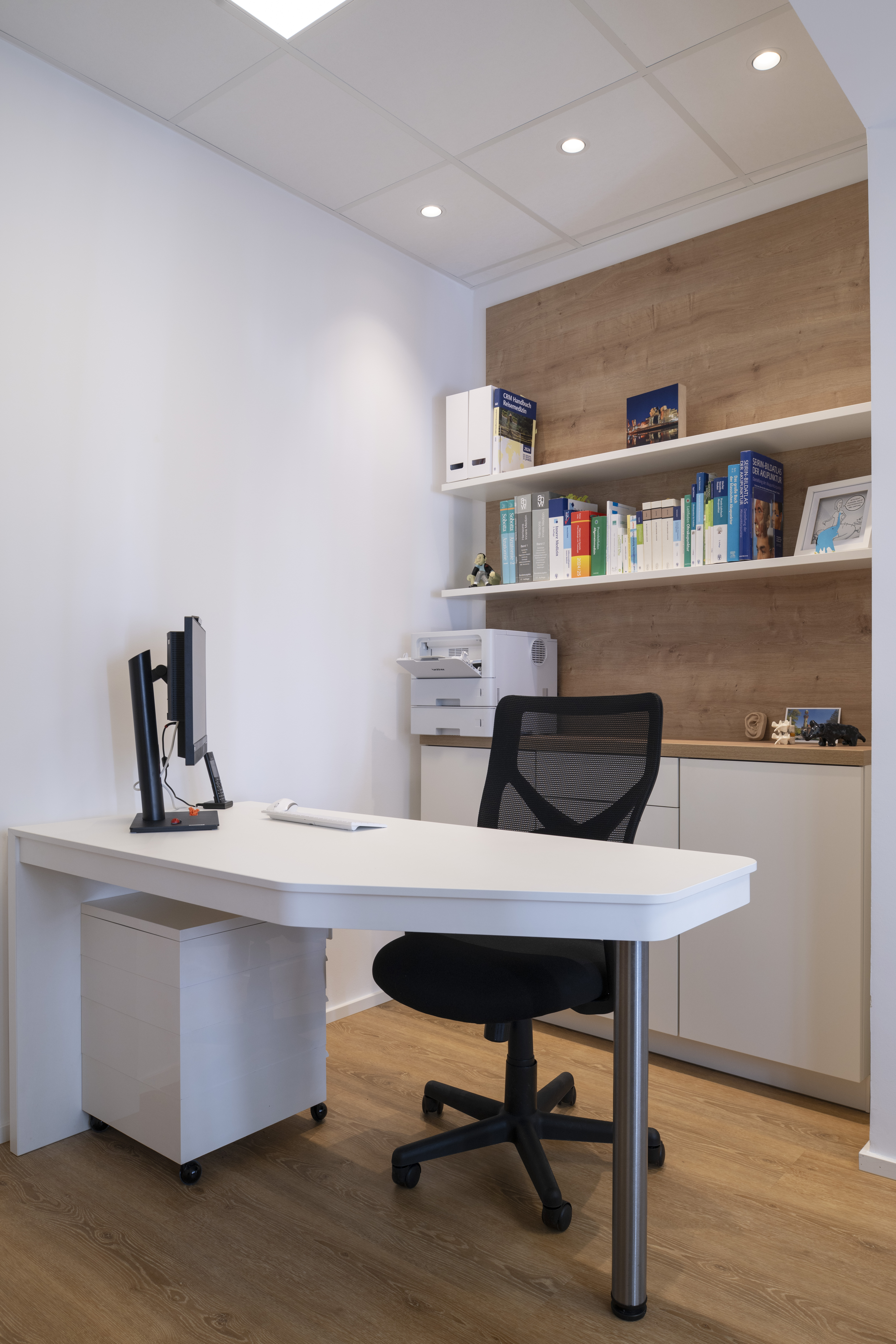 Leerer Büroraum mit weißem Schreibtisch, schwarzem Stuhl und Bücherregal