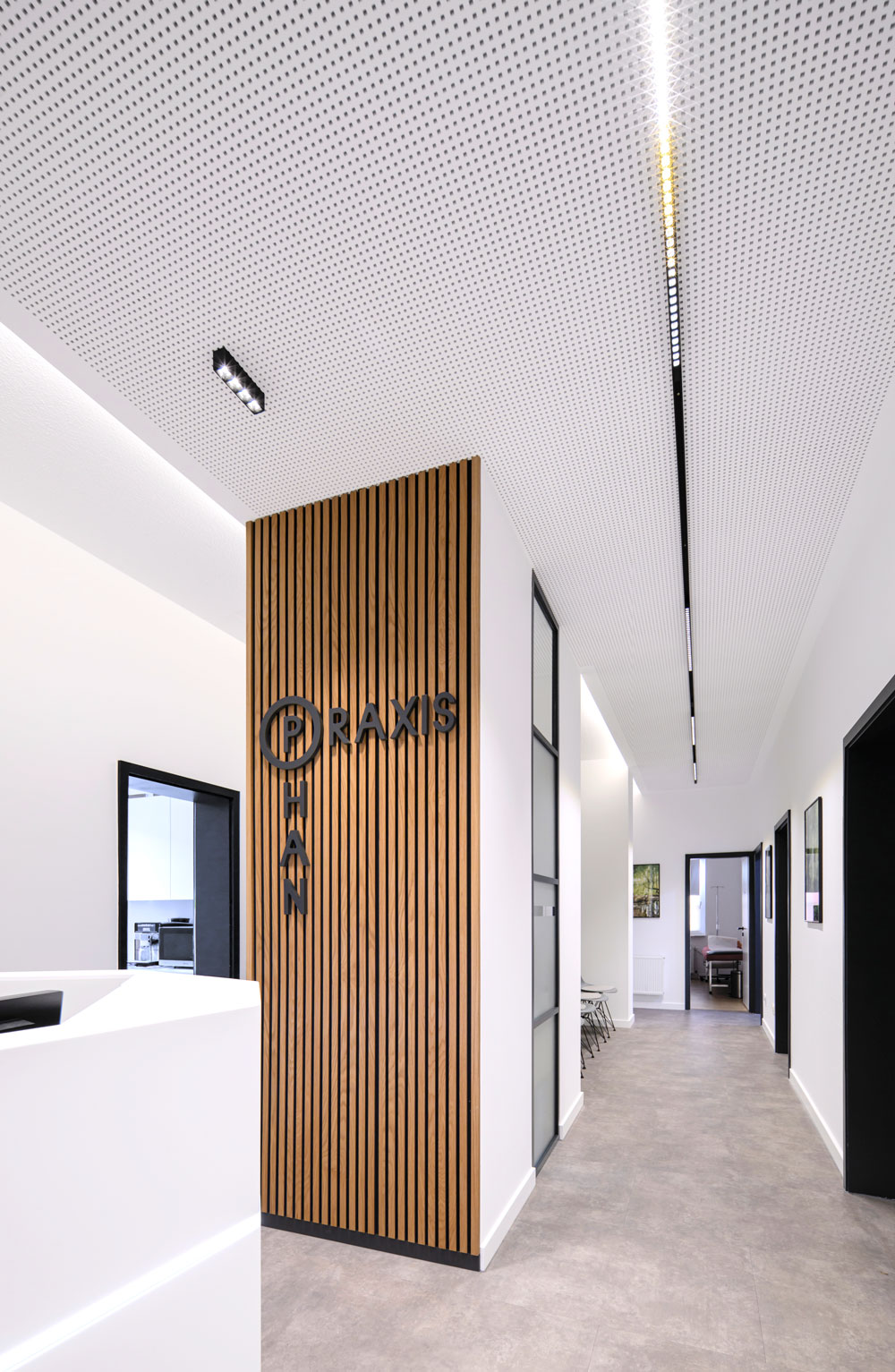 Heller Flur mit Holzlamellenwand Praxis Schriftzug und weißen Wänden