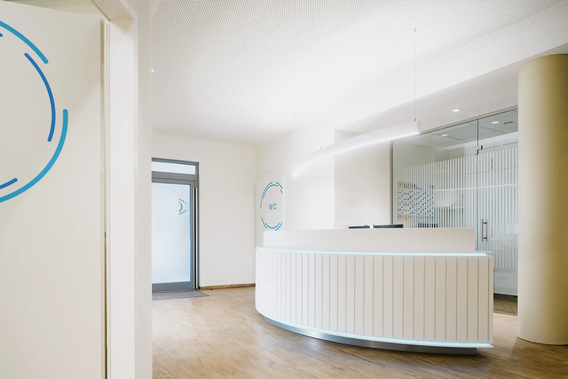Heller Empfangsbereich mit weißer runder Theke und blauen Wandlogos
