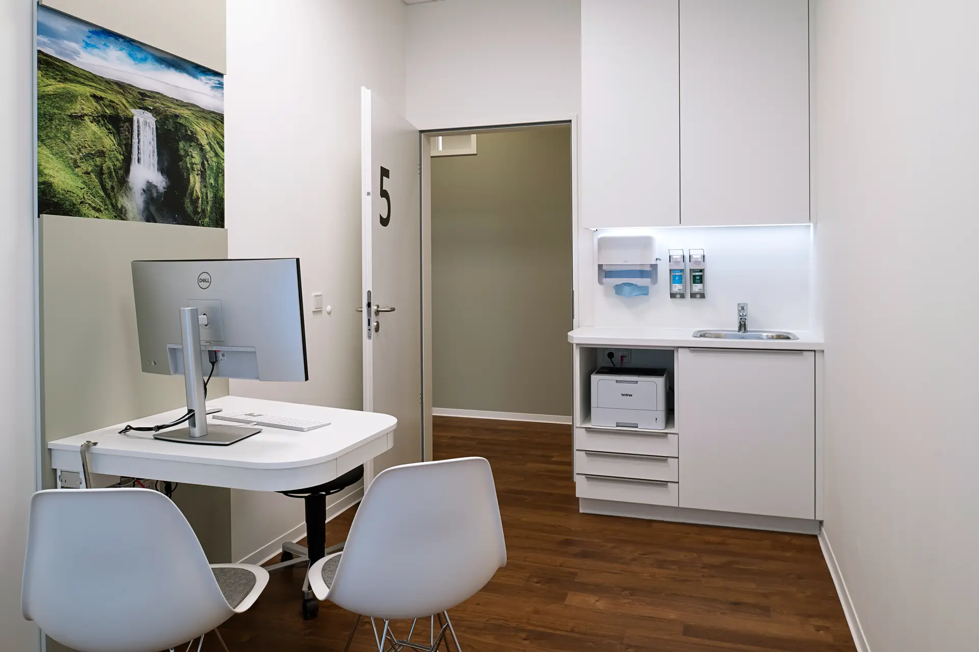 Leerer Behandlungsraum in Weiss mit Tisch, Stuehlen, Monitor und Spuele
