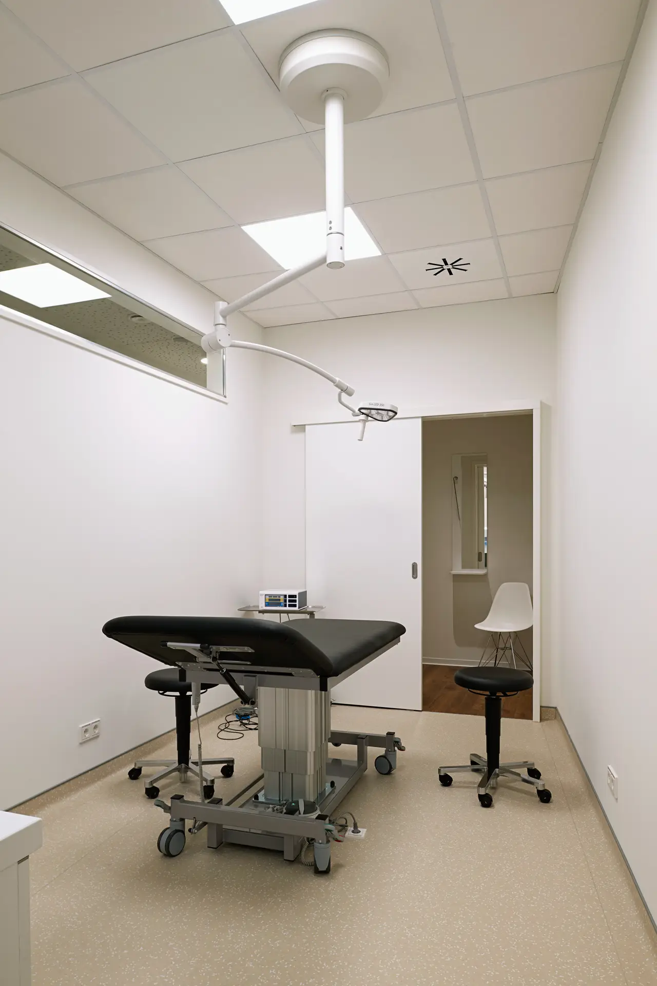 Leerer weißer Behandlungsraum mit schwarzer Liege und OP Lampe