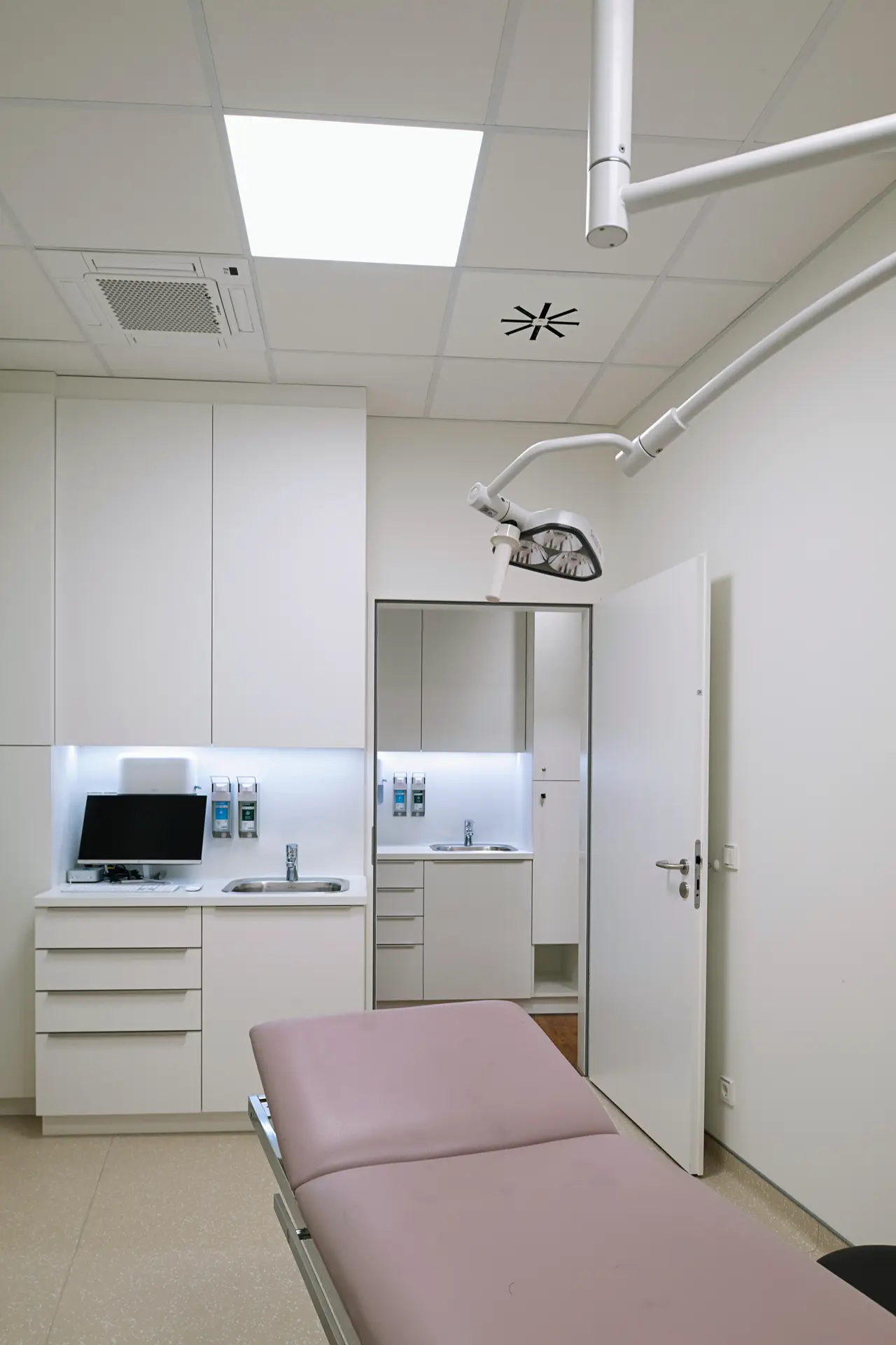 Leerer heller Behandlungsraum in Weiß mit rosa Liege und OP Lampe