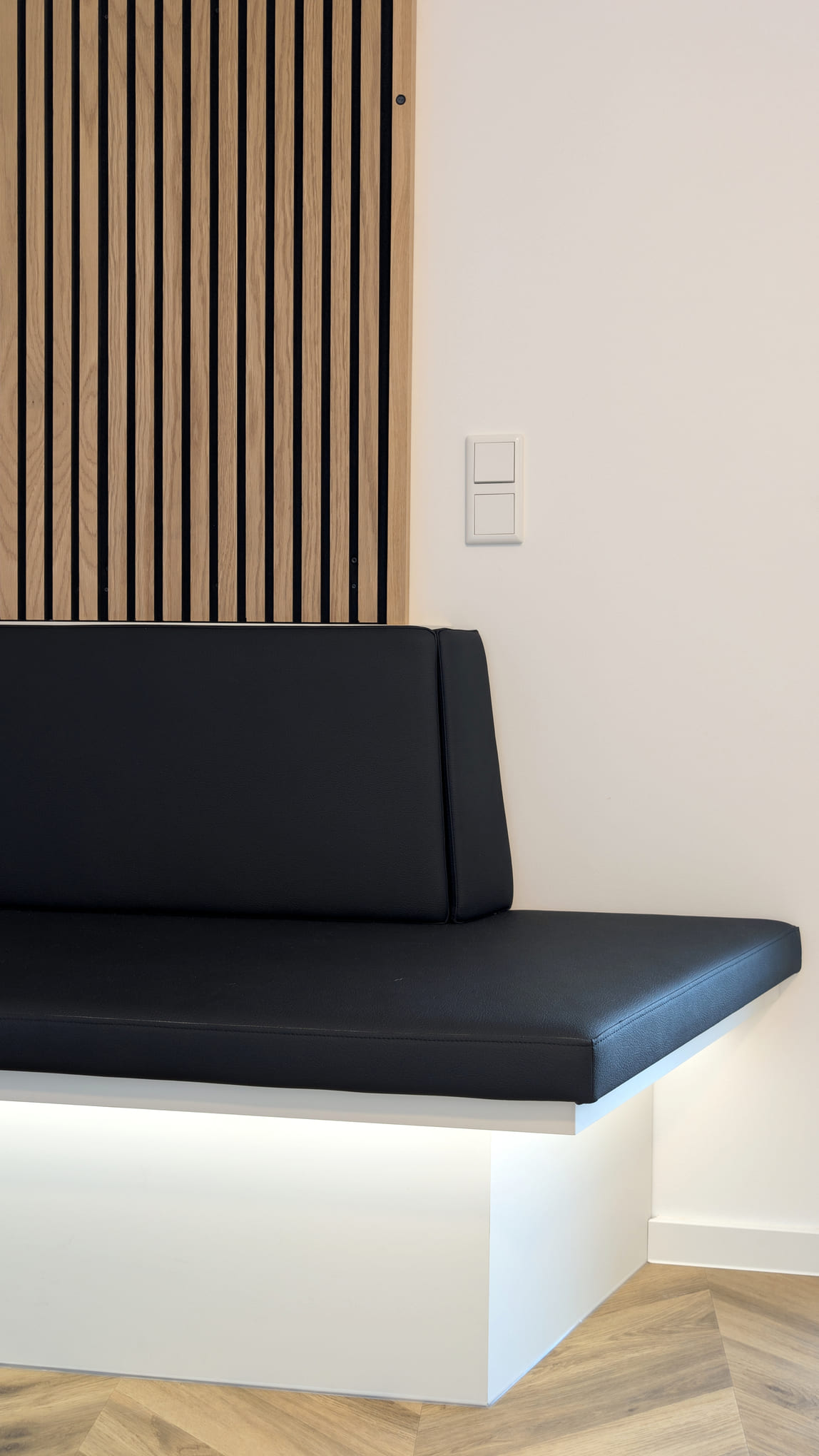 Schwarze Sitzbank mit indirekter Beleuchtung vor einer Holzlamellenwand