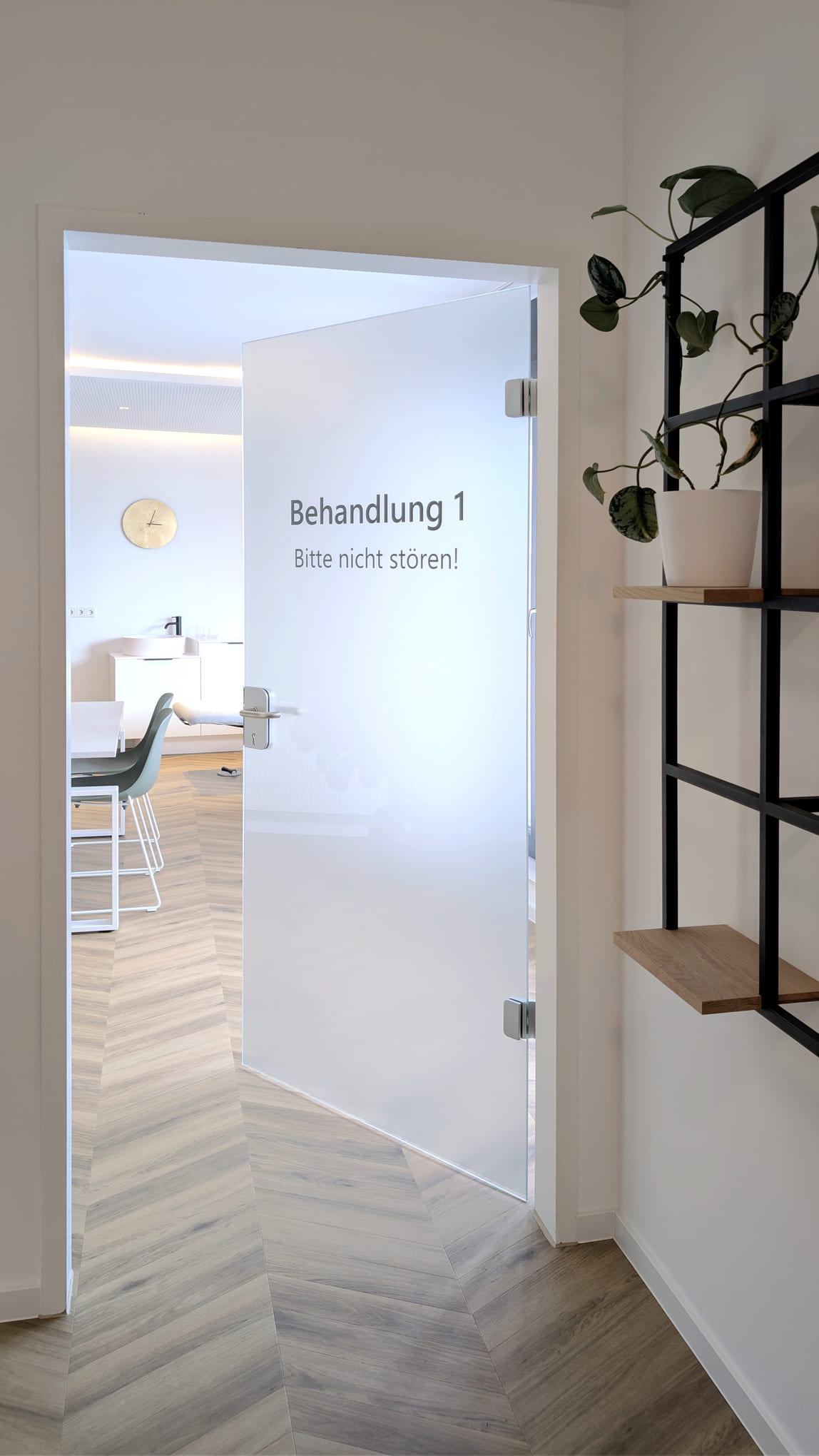 Milchglastuer mit Aufschrift Behandlung 1 neben einem Regal mit Pflanze
