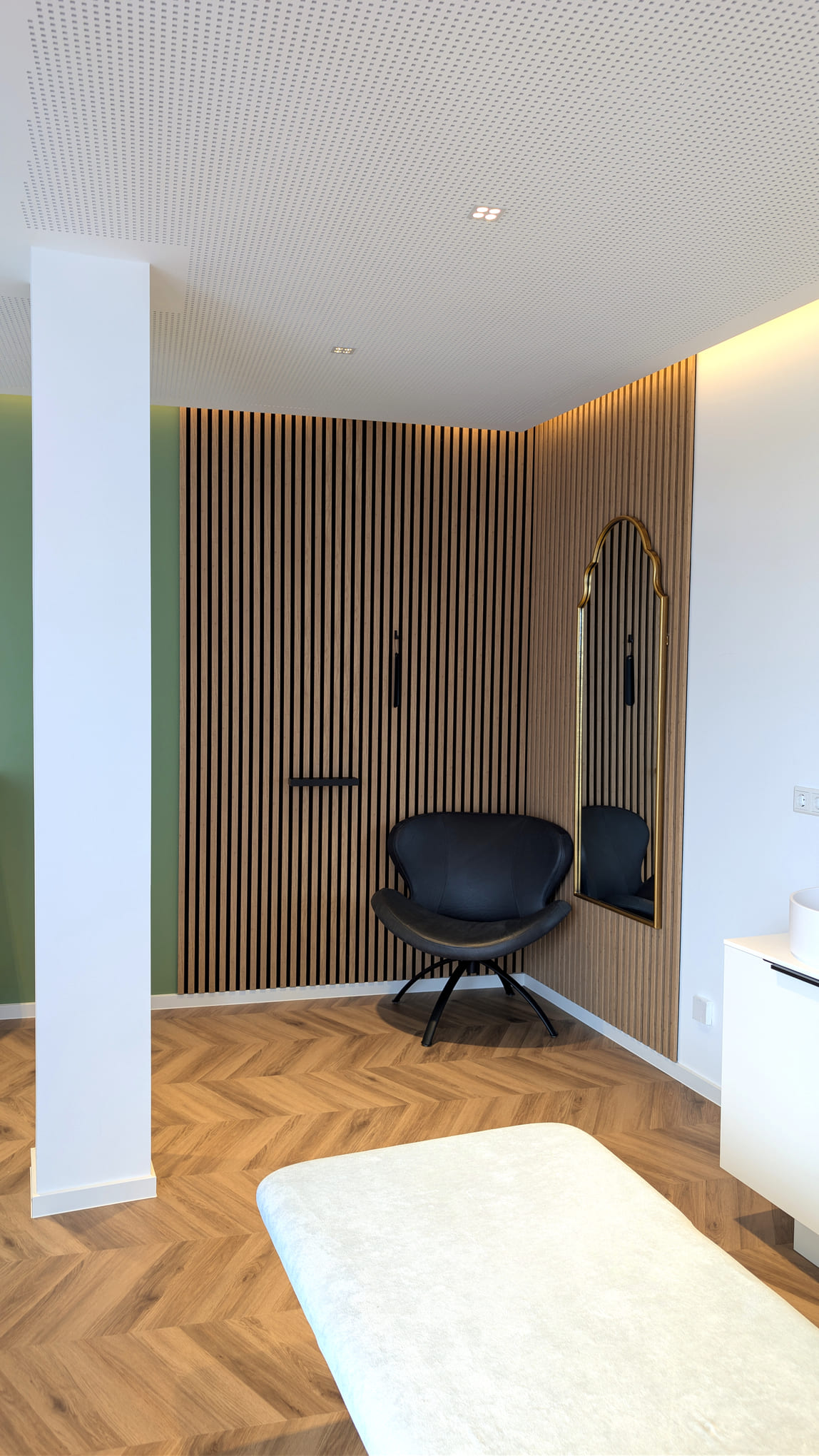 Moderner Raum mit schwarzem Sessel Holzlamellenwand und goldgerahmtem Spiegel