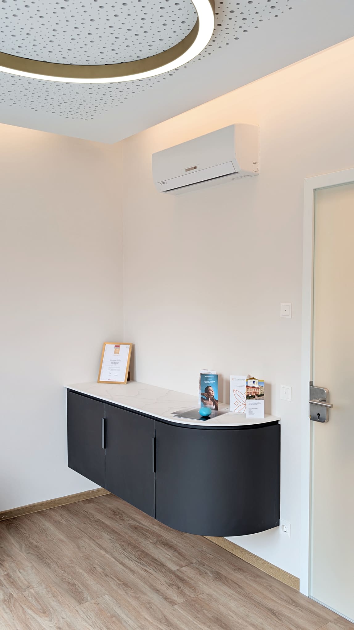 Moderner Praxisraum mit anthrazitfarbenem Sideboard Klimaanlage und Broschueren