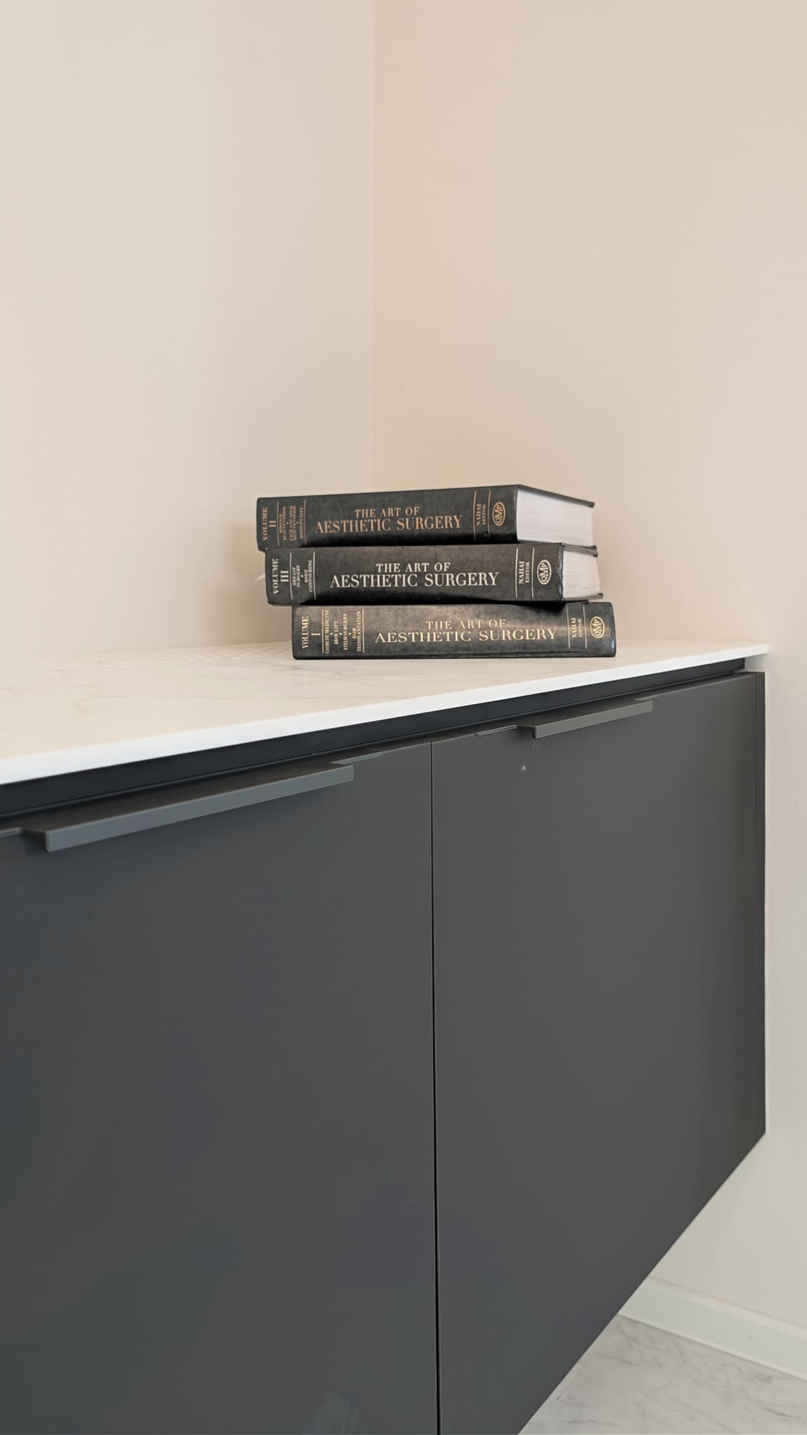 Drei schwarze Fachbuecher ueber aesthetische Chirurgie auf einem Schrank